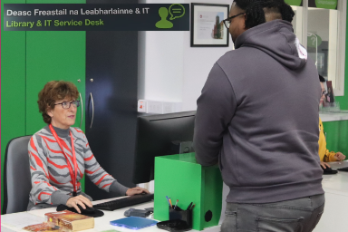 Image of iLibrary & IT Help desk. A staff member assists a student.